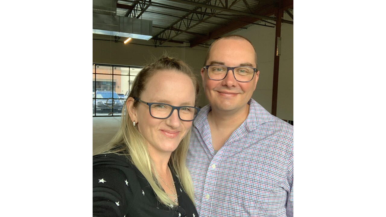 A selfie image if a man and a woman smiling for a photo in an empty storefront.