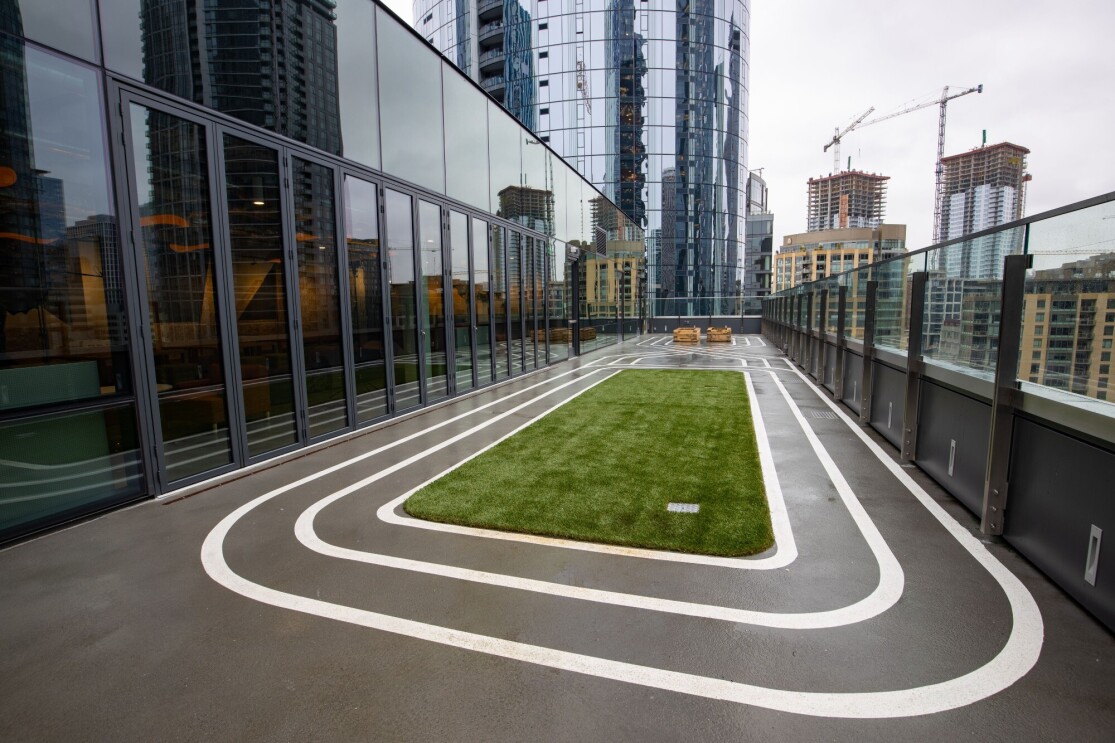 An image of an outdoor area on the rooftop of the Mary's Place Family Center in The Regrade. There is a small turf field with white track lines encircling it.
