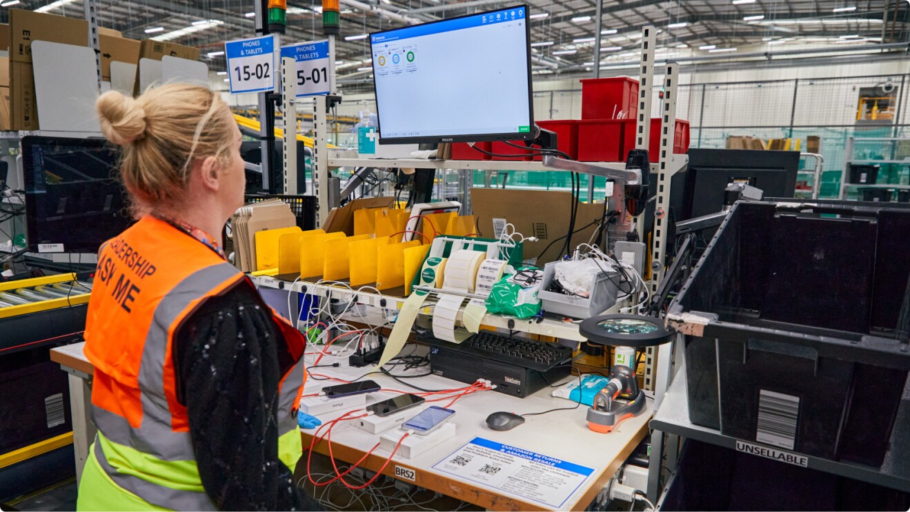 Amazon warehouse worker in orange safety vest at workstation