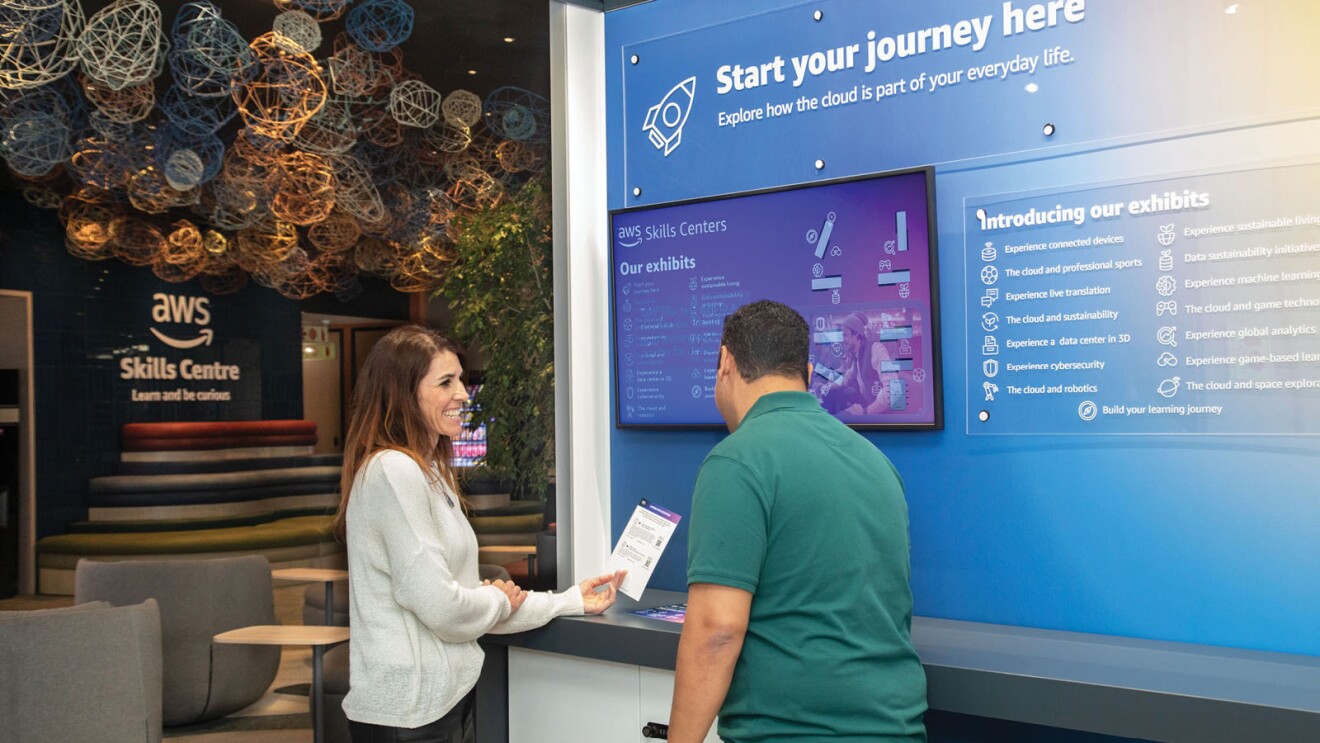 side view of a woman smiling as she holds up instructions and shows them to a man at the cloud discovery space in the new aws skills center in cape town south africa