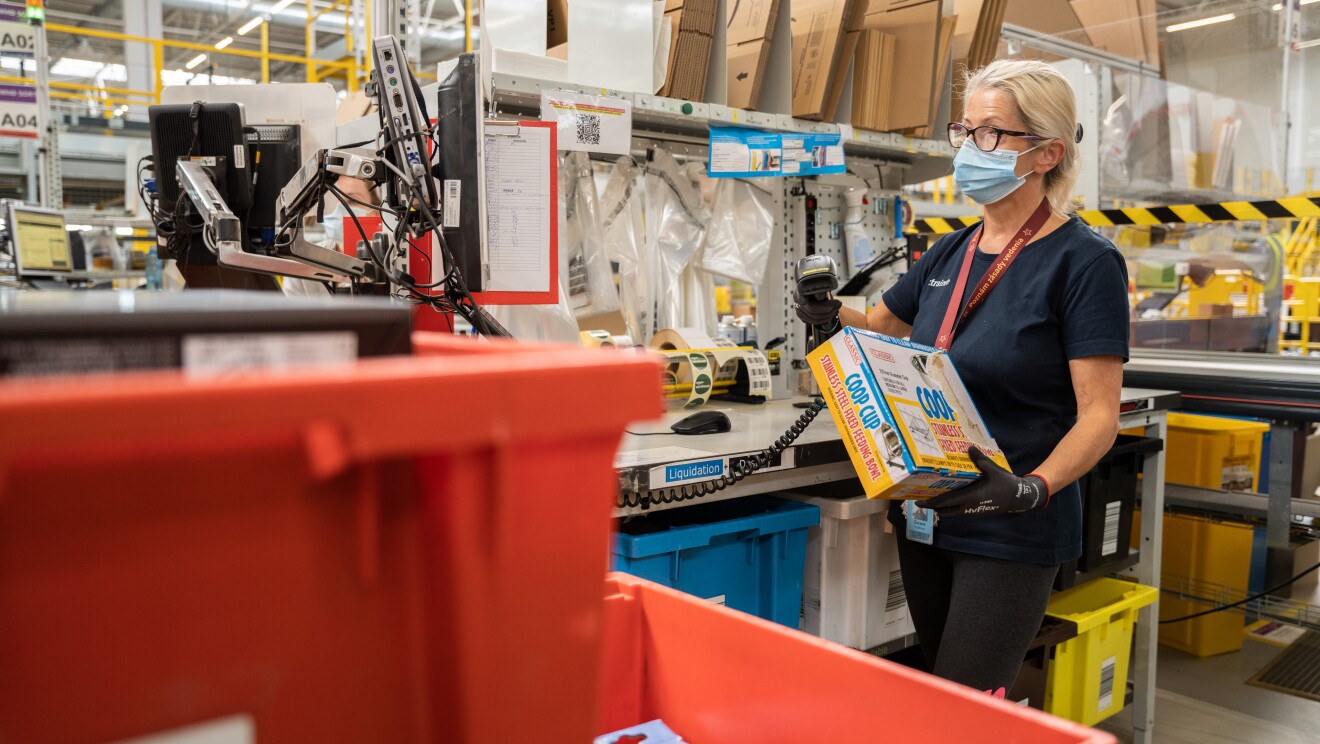L'immagine mostra una dipendente amazon all'interno del magazzino che controlla i prodotti resi