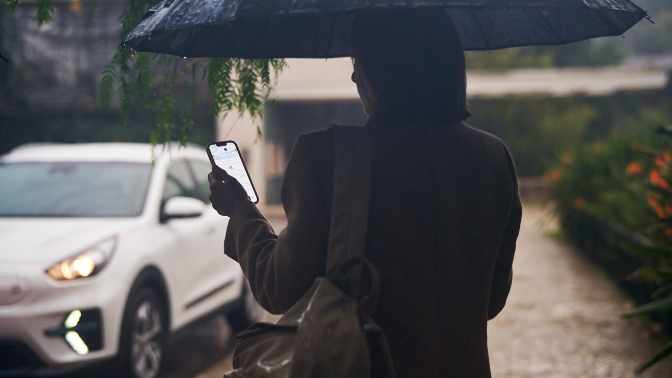 A customer standing outside reviewing the Uber app on their phone, with a car approaching in the street.