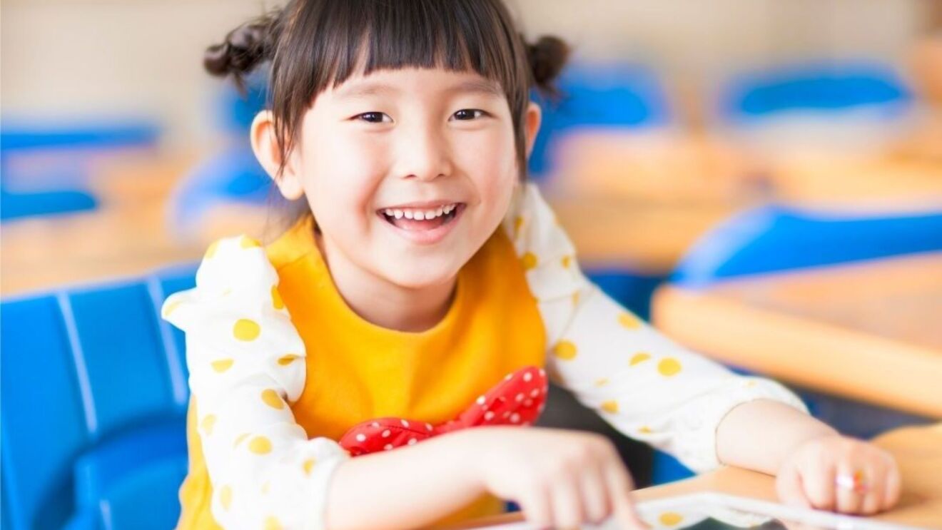 微笑的学步女孩坐在写字台上拿着平板电脑。
