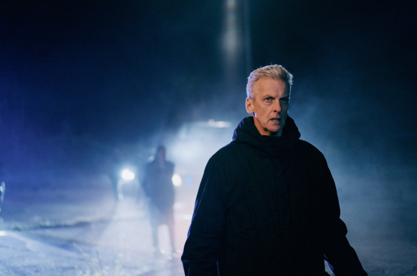 An elderly man wearing black stands in the street