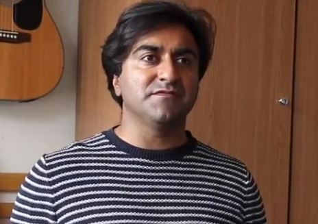  Adi Latif wearing a stripey jumper and looking straight into camera from his home in Camden, London