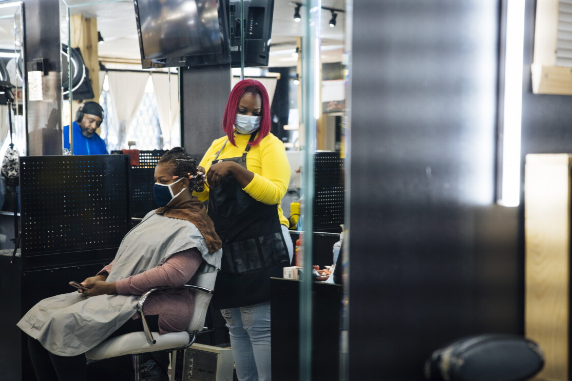 Inside her salon, Auhzha Wright styles a client's hair while both are wearing face coverings