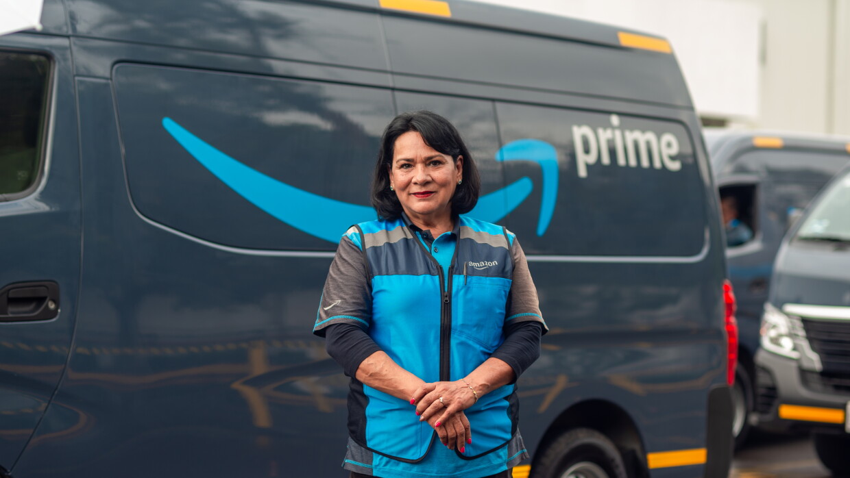 Mujer vestida con el chaleco de Amazon delante de una furgoneta con el logo de Prime. 