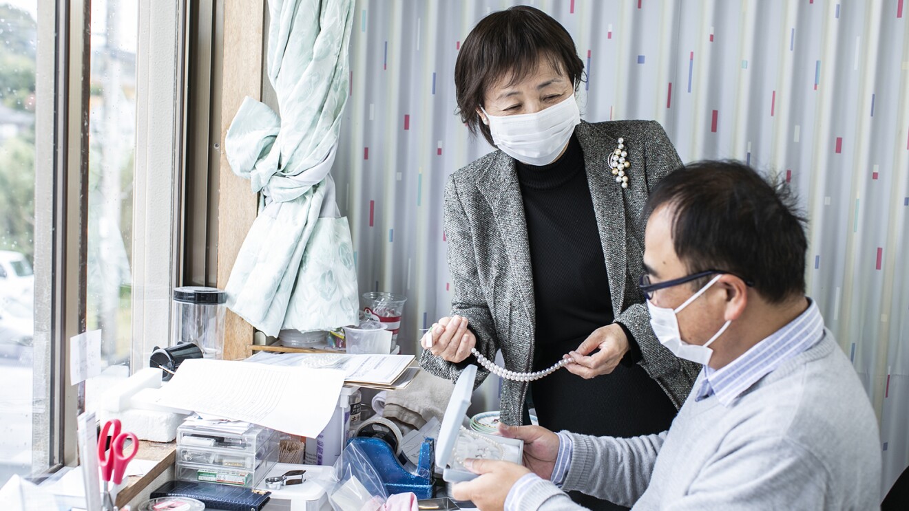 真珠を手に従業員と話をする磯和恵子さん