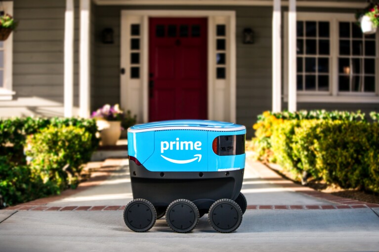 A small blue delivery bot with Amazon Prime branding sits on a walkway that leads to a house.