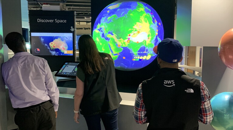 three people stand looking at a display with a large globe.