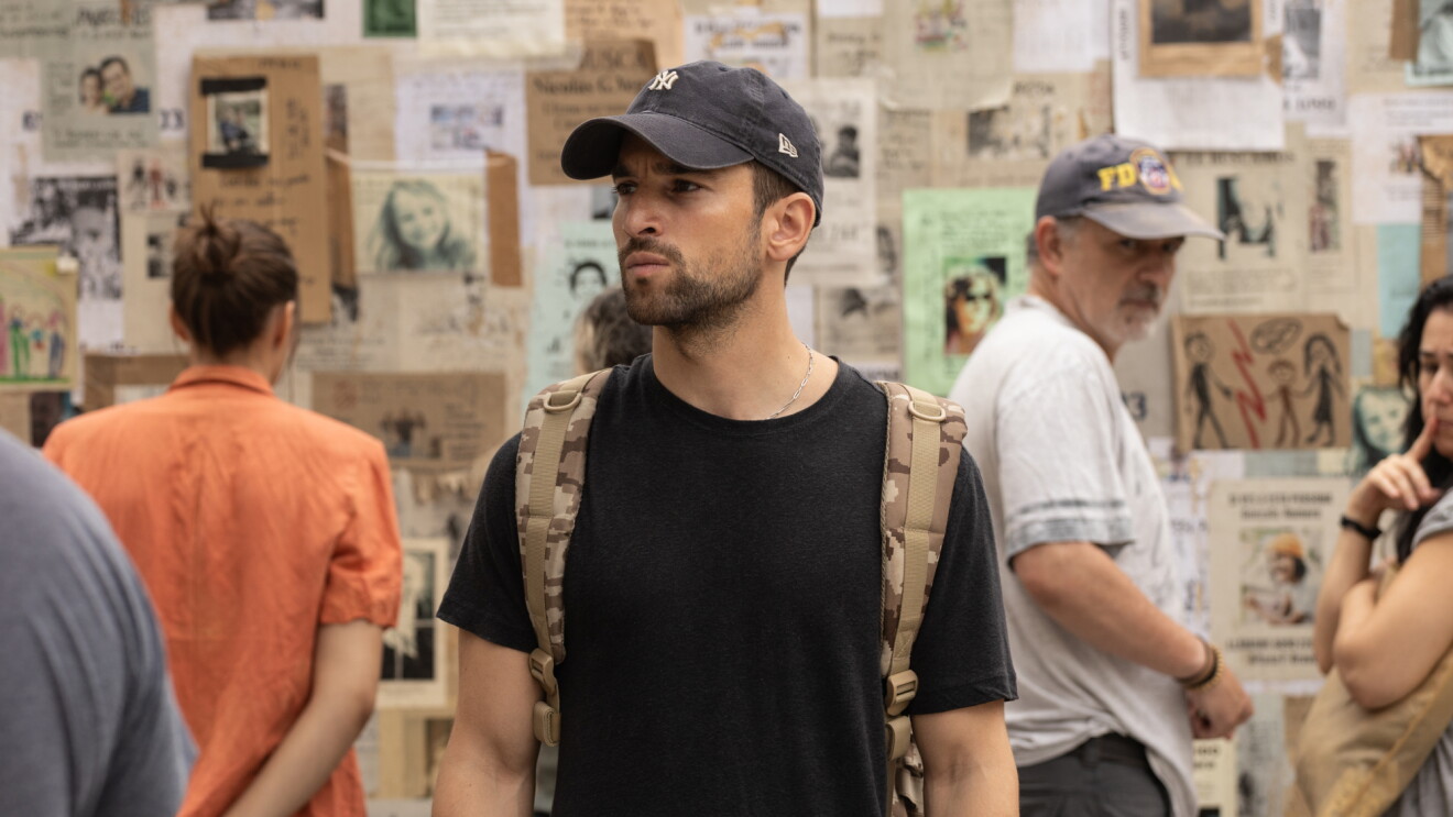 Man stands in a room surrounded by pictures of people on the wall