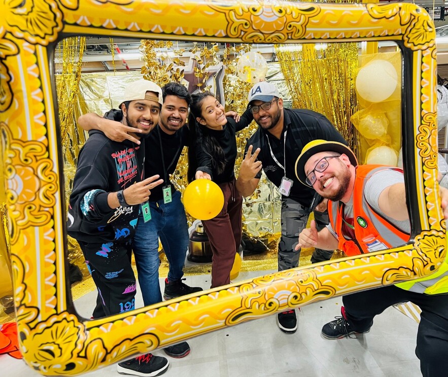 Vier Mitarbeiter:innen vom Sortierzentrum Schönefeld sind in Pyjamas und schauen durch einen Bilderrahmen.