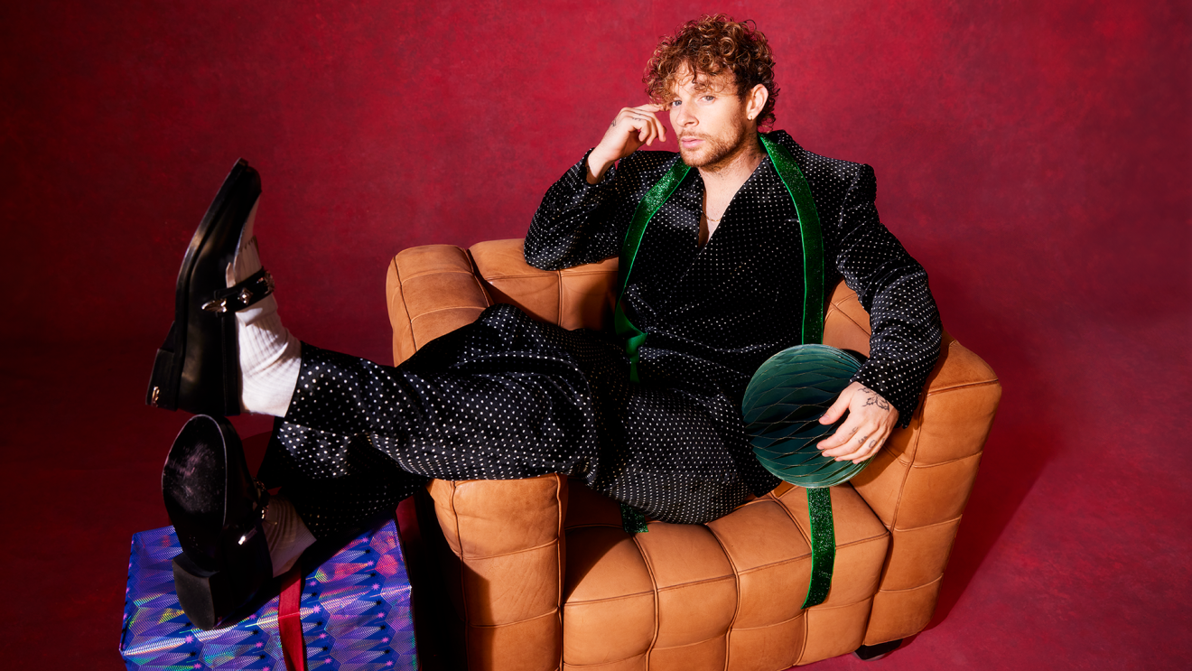 Tom Grennan sitting across a brown armchair with a Christmas gift