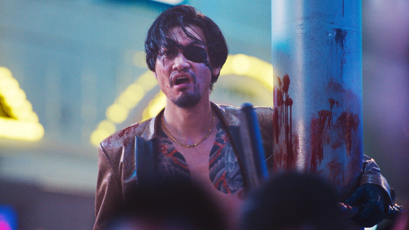 黒いアイパッチをして、血まみれの大きな筒を抱えている男性。胸にカラフルな入れ墨があり、その上に革のジャケットを着ている