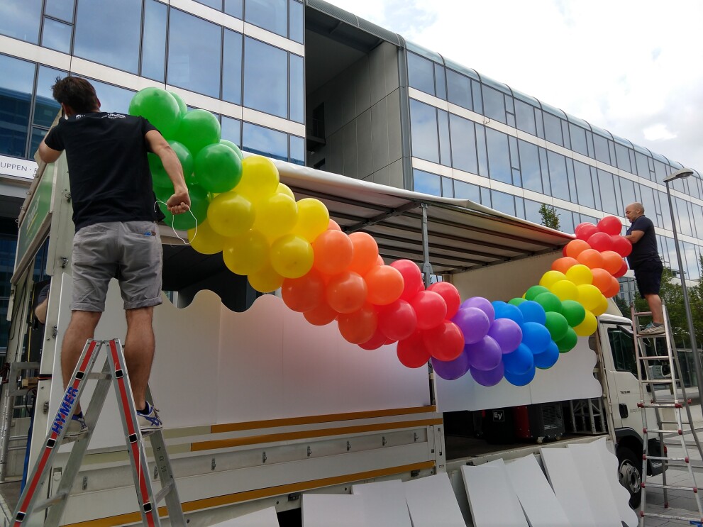 Zwei Männer stehen auf Leitern und befestigen Luftballons am Glamazon-Wagen.