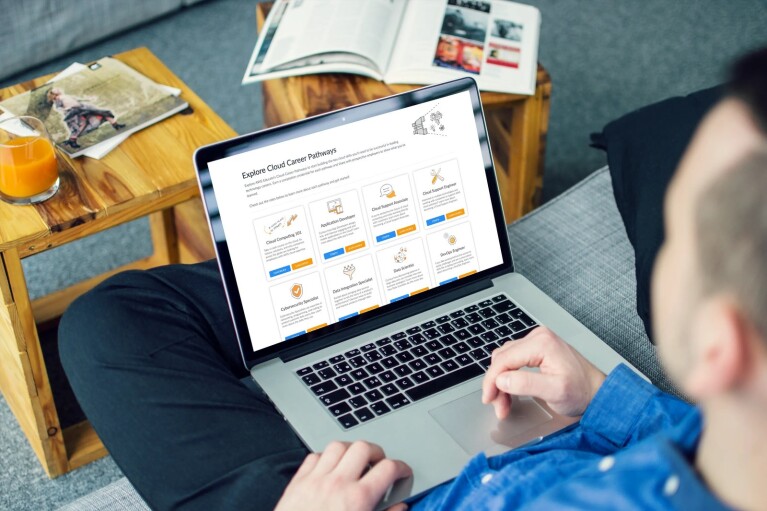 A man sitting on his laptop using the Amazon Educate programmes. In front of him is a wooden table with a drink and magazine.