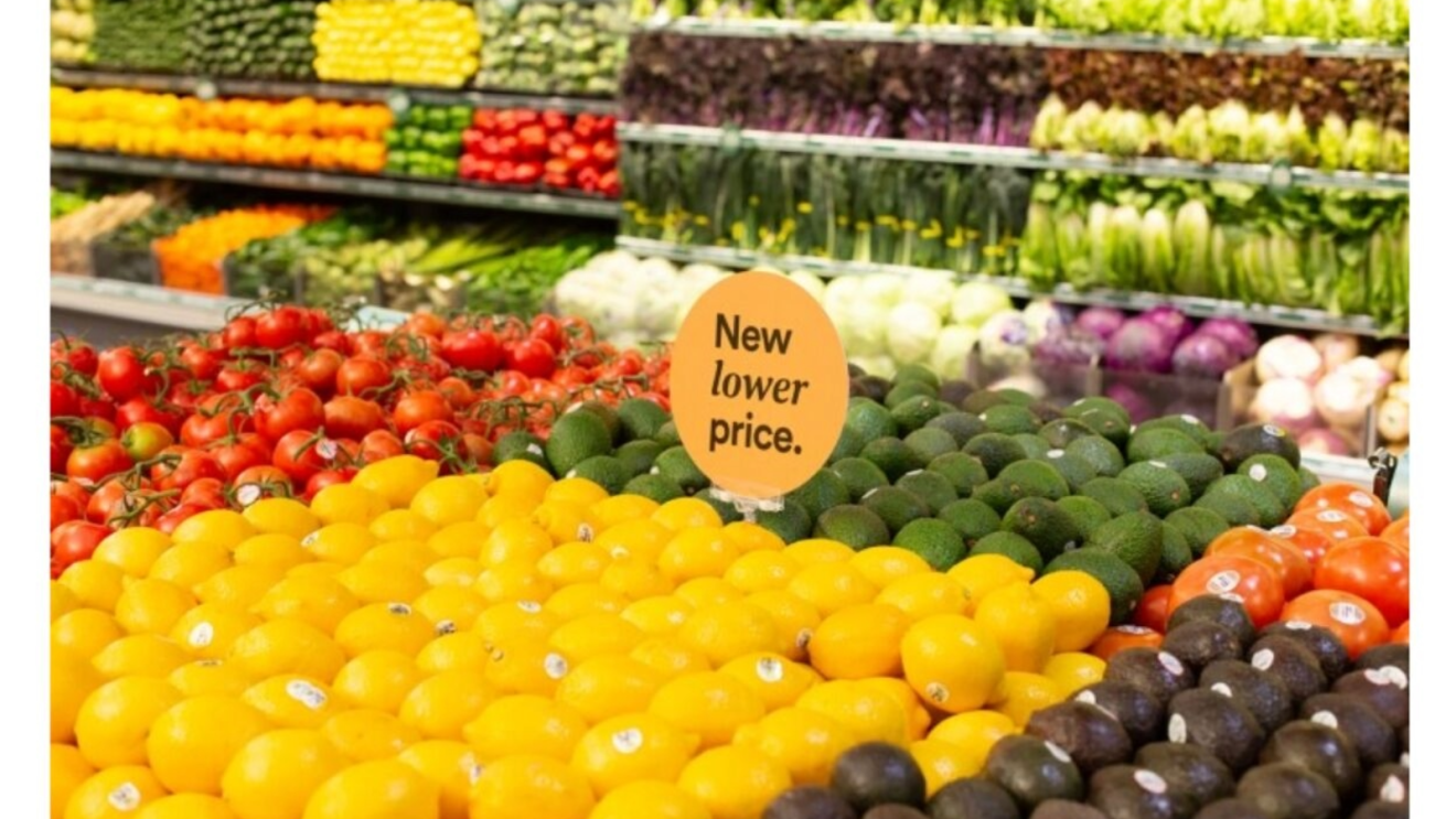 Colorful produce display in grocery store with 'New lower price' sign