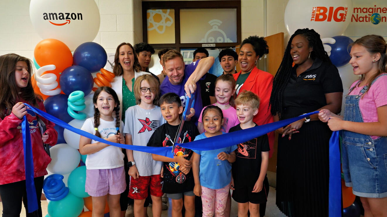 Group celebrating Amazon event with balloon arch and ribbon cutting
