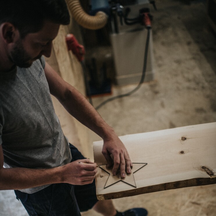 Ein Mann zeichnet einen Holzstern auf einer Holzplatte nach. Er schaut konzentriert auf den Stift in seiner Hand.