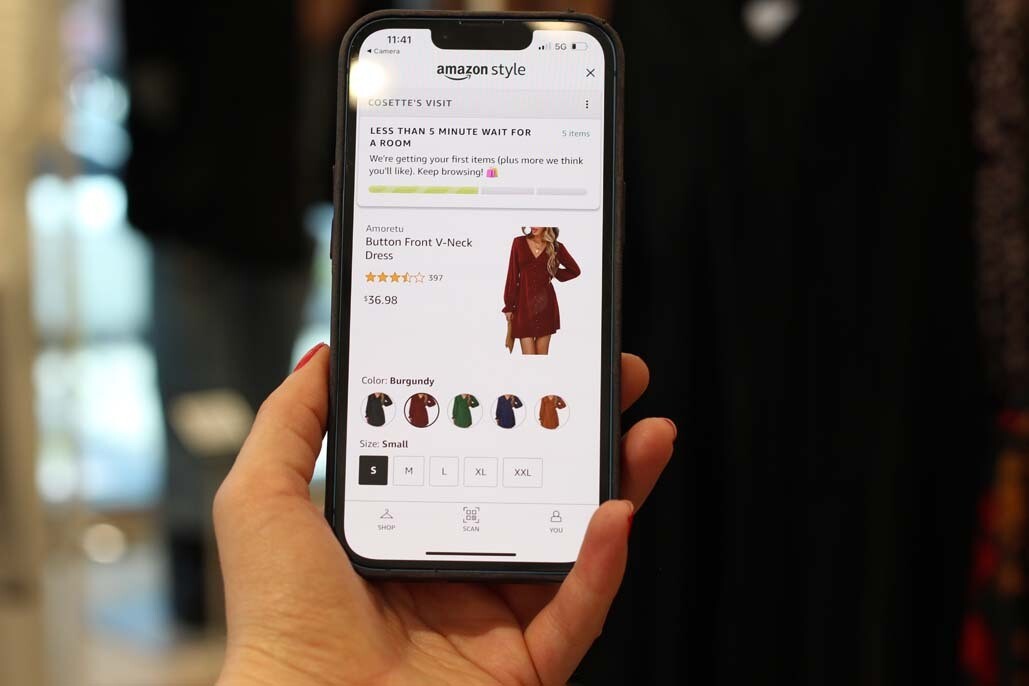 An image of a hand holding a phone in the Amazon Style store. On the screen is the product detail page on Amazon for a dress.