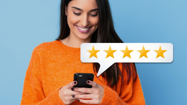 Eine Frau mit orangenem Pullover schaut auf ein Handy.