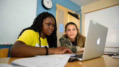 An image of two young women working together on a laptop in a classroom.