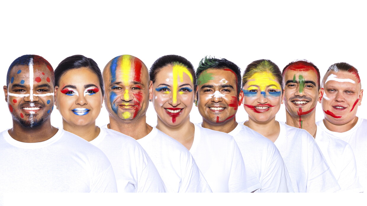 Para el Día de la diversida Amazon ha preparado una acción con asociados de diferentes países que llevan la bandera pitnada en su cara. En la foto, con camiseta blanca 8 trabajadores de Amazon con una camiseta blanca y mirando sonriendo a cámara.  Ángel, Ingrid, Adrián, Giselle, Ricardo, Gladys, Mohamed y David. 
