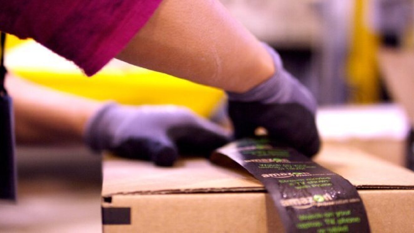 Dos manos con guantes colocan la pegatina para cerrar una caja de Amazon.