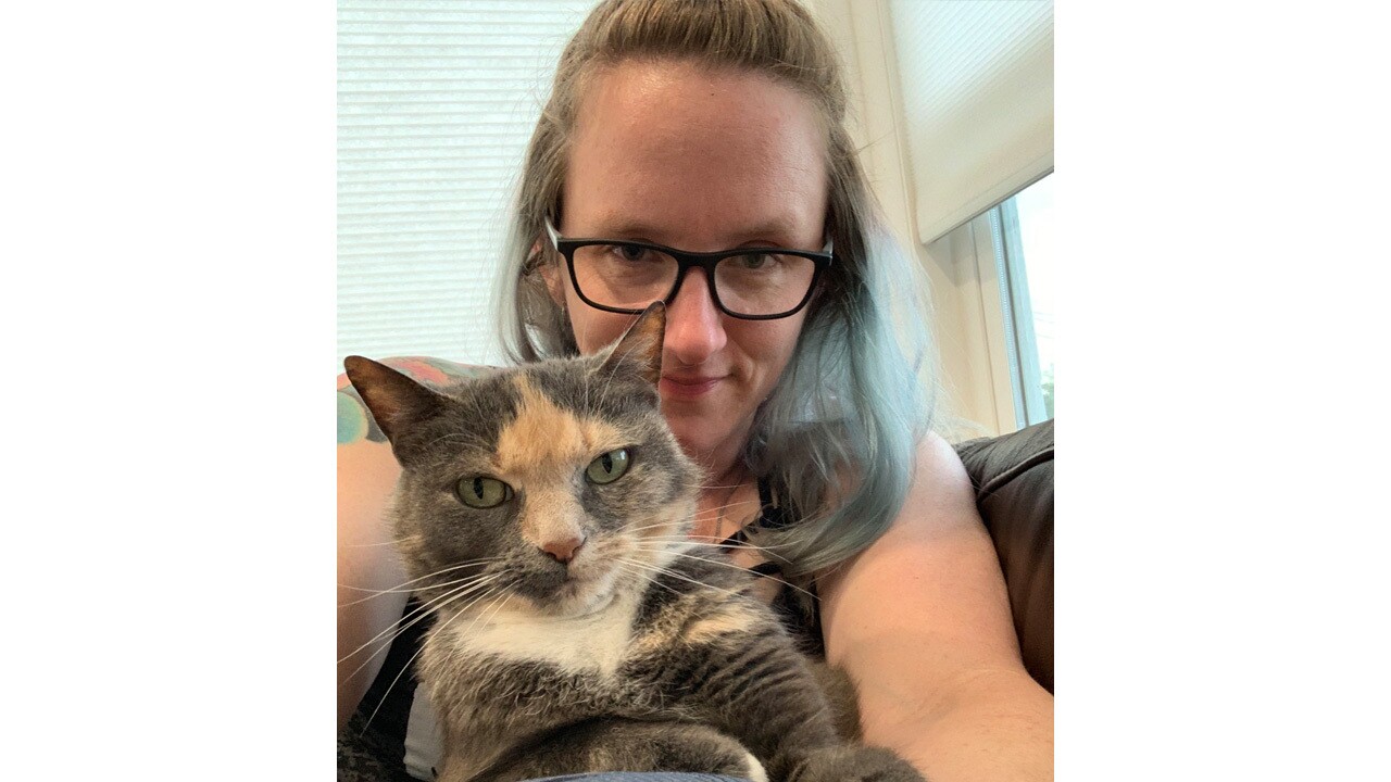 An image of a woman sitting on her couch taking a selfie with her cat.