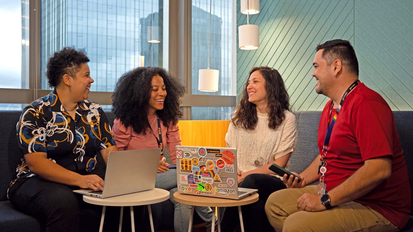 Grupo de 4 pessoas conversam. Eles estão na frente de dois computadores
