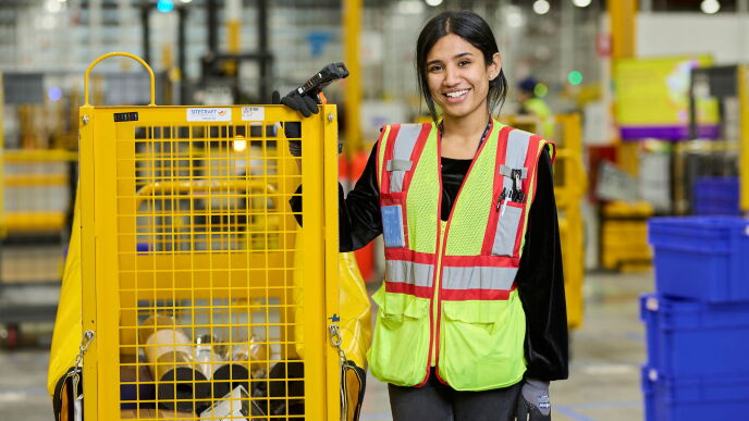 Amazon fulfilment centre team member in a high vis jacket standing with a cart of items