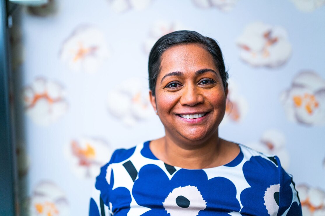 An image of a woman smiling for a headshot photo. Behind her is wallpaper with large pieces of popcorn pictured on it.