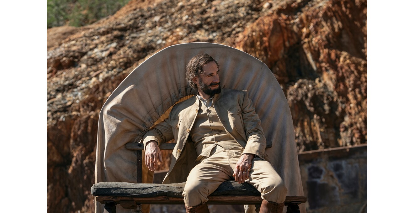 茶色い地層の屋外で、ホロ場所の荷台にもたれかかる男性。