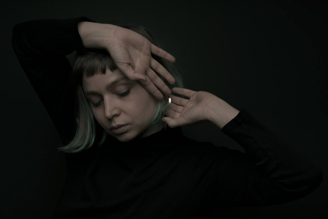 Alice Gosti poses with her hands framing her face as she looks down from the camera.