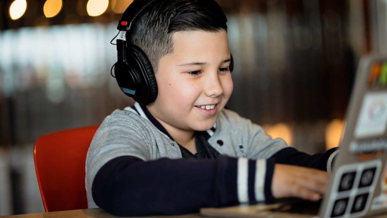 一个微笑的男孩戴着耳机在笔记本电脑上打字。