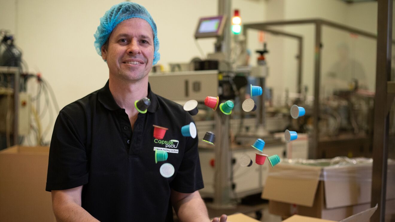 A man throws several coffee capsule packs up in the air in a manufacturing facility