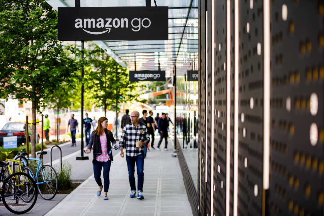 A man and a woman walk in front of the Amazon Go store in Seattle, WA.