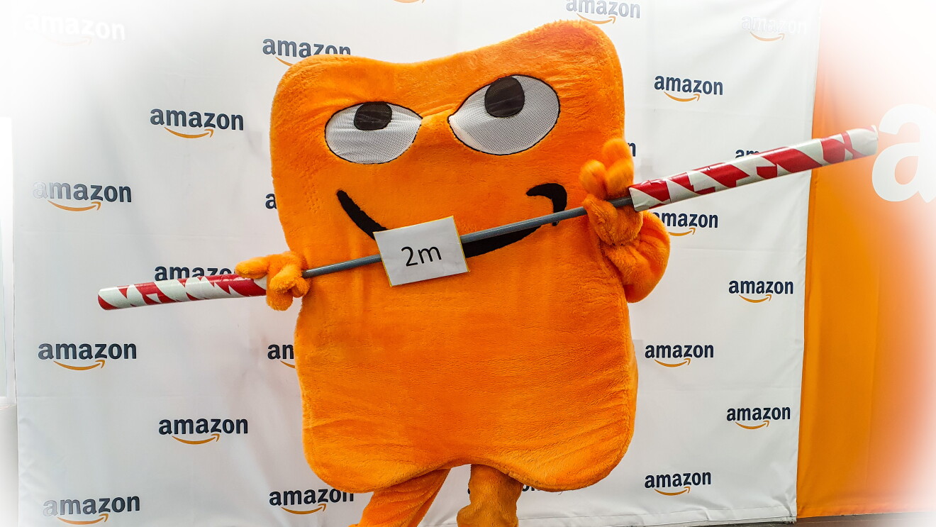 Pecci, das Amazon Maskottchen in Lebensgröße, ähnelt einem orange-farbenen Paket mit dem typischen Amazon Smile-Lächeln.
