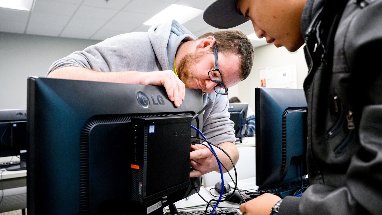 A photo of two students at Blue Mountain Community College adjusting Ethernet cables on a desktop computer.