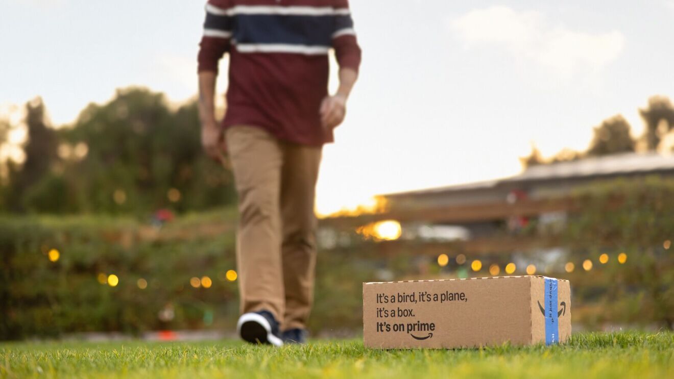 Amazon box on grass with person walking by at sunset.