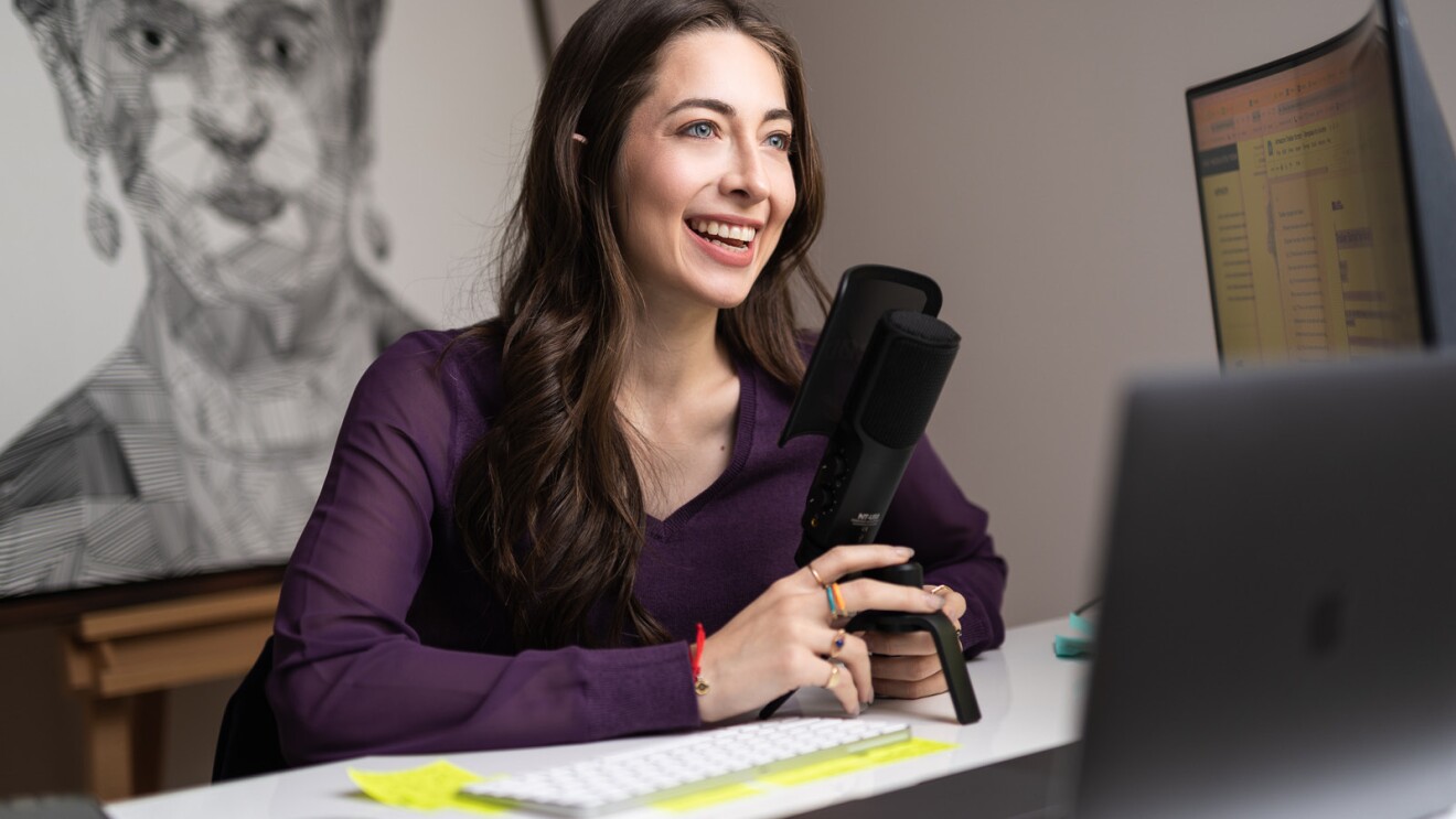 A photo of This is Small Business host and producer Andrea Marquez speaking into a microphone at her desk. 