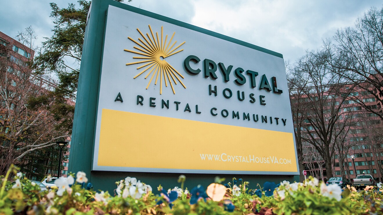 一个建筑前的标志,上面写着“水晶房子:一个租赁社区”,底部是该建筑的网站(www.crystalhouseva.com)。