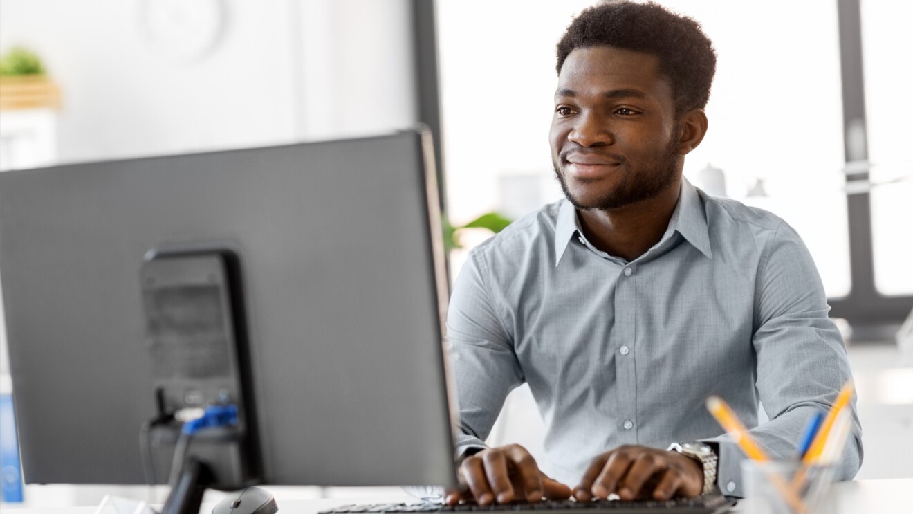 A man sits in front of a computer monitor smiling while he types.