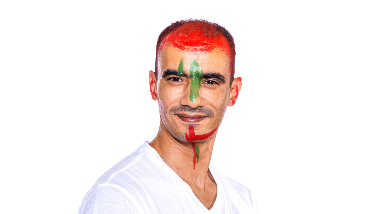 Para el Día de la diversida Amazon ha preparado una acción con asociados de diferentes países que llevan la bandera pitnada en su cara. En la foto, Mohamed con camiseta blanca, mirando sonriendo a cámara con la bandera de su país puntada en la cara. Tiene el pelo oscuro corto y se le entreve el bigote. 