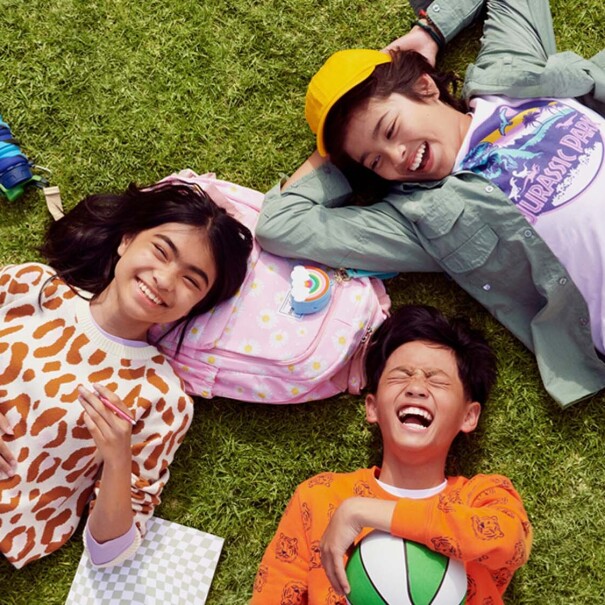 Image of three kids lying on grass with school supplies scattered around them.