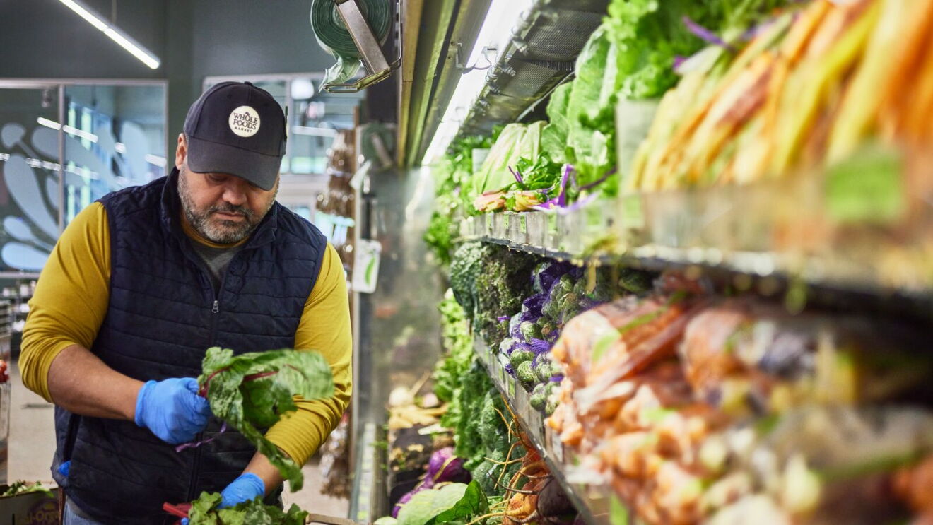A Whole Foods Market employee stocks the produce section.