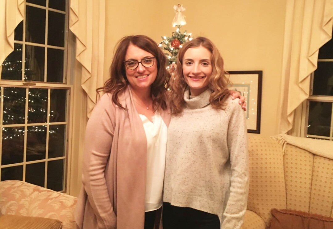 An image of two women smiling for a photo in front of a Christmas tree in their living room.