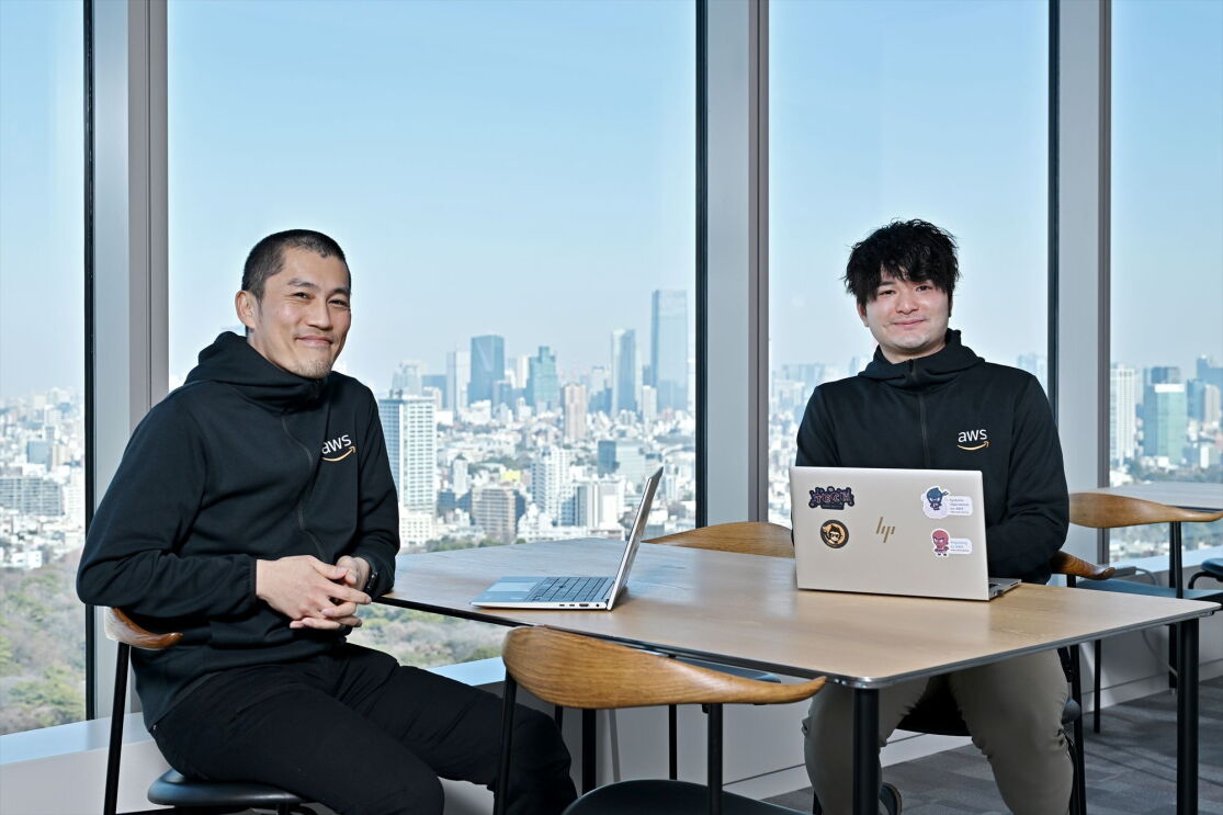 髪がない男性と巻き毛の男性は前を向いて笑顔でいる。室橋さんと杉山さん