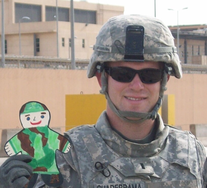 Aaron Guaderrama in combat uniform, holding a child's paper cutout of a soldier in camouflage