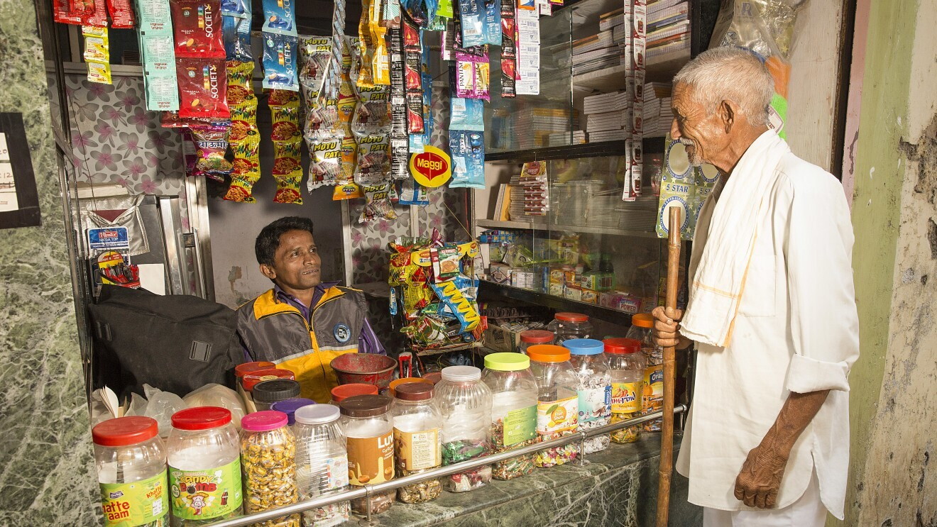 Image of an old man standing opposite to a shop keeper who is seen seated in his shop
